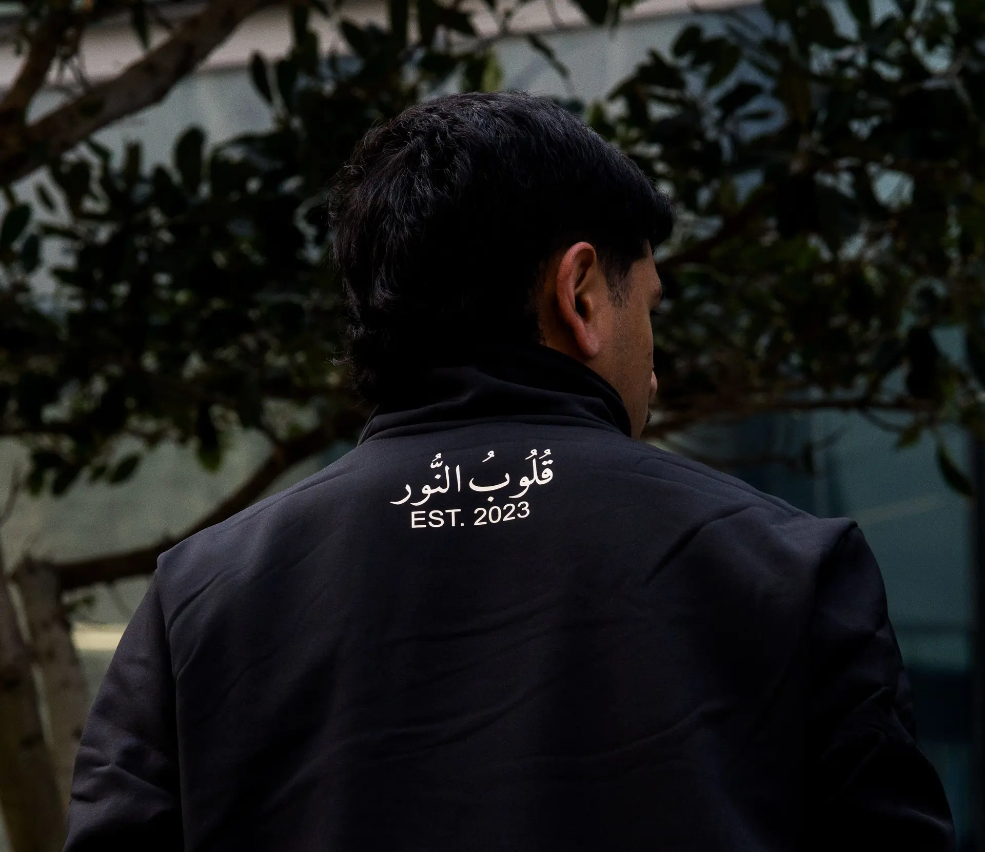 Black soft shell from behind, Arabic across the shoulders